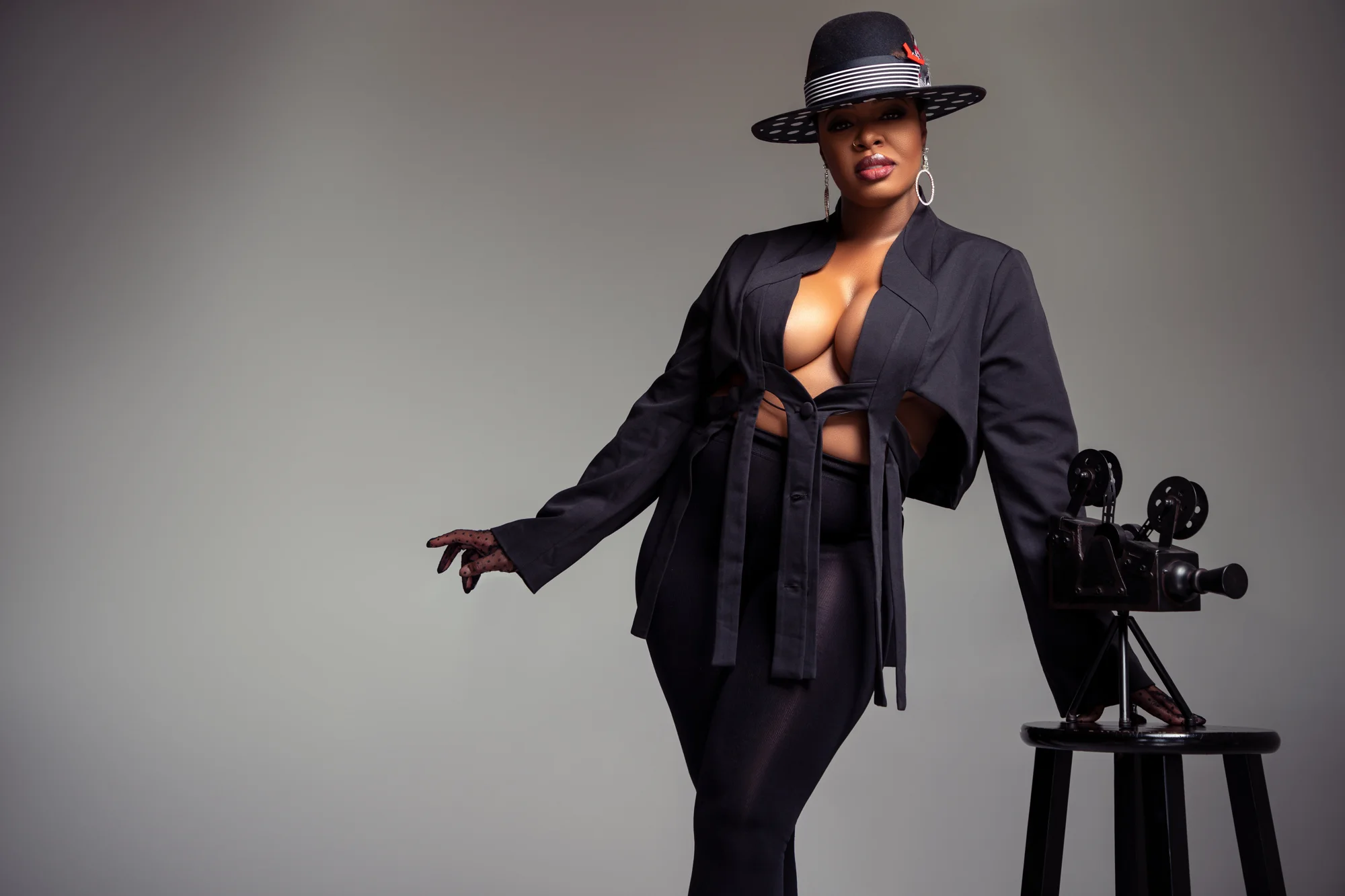 Ta'Rhonda Jones in a black suit and hat beside a vintage film camera
