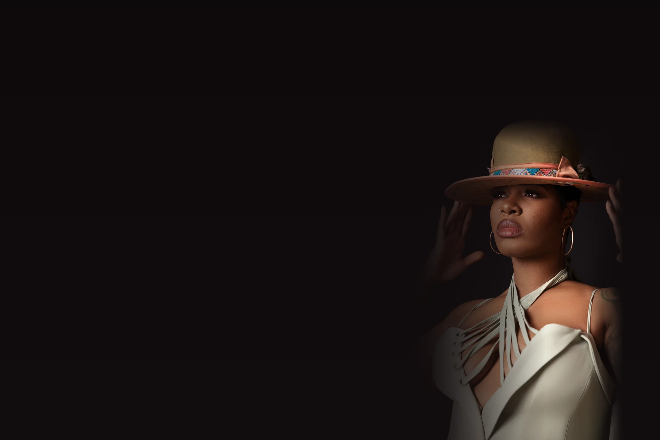 Ta'Rhonda Jones with both hands on the brim of her hat, looking up